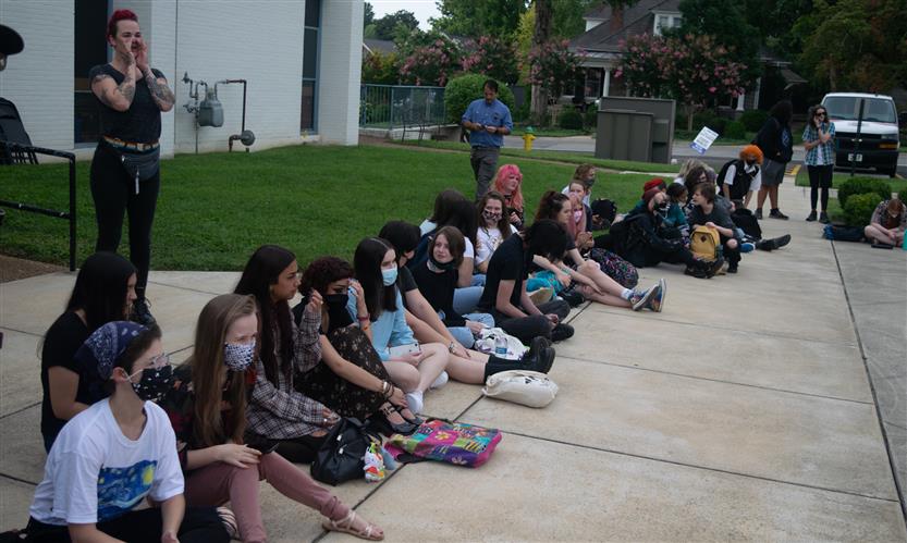 A group of students sit on the sidewalk outside of their school